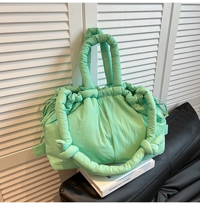 Detail of mint green quilted tote bag with drawstring and padded handles on white books