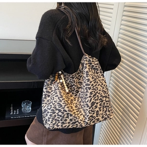 Detail of leopard print tote bag featuring thin brown straps and wooden bead charm