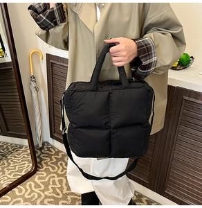 Detail of black quilted puffer bag showing thick handles and adjustable shoulder strap