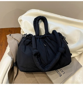 Close-up of black quilted puffer tote bag featuring padded handles and side knot details