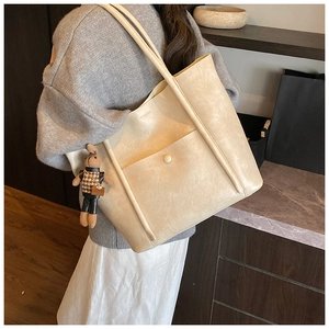 Detail of cream tote bag with fine leather texture and cute rabbit charm on model
