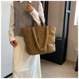 Brown puffer tote bag with quilted pattern and fashion label held by a model