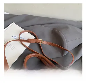 Detail of adjustable shoulder strap with gold metal buckle on brown leather bag