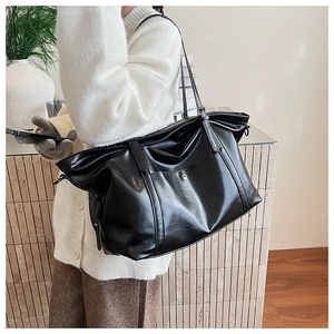 Model wearing a large black glossy tote bag with side straps and studded front pocket
