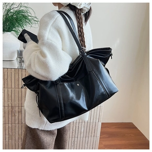 Detail view of large black leather tote bag with side drawstrings and shoulder straps