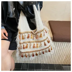 Close-up of white knit tote bag featuring golden embroidery and multi-color tassels