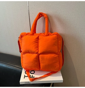 Close-up of orange quilted puffer tote bag on a book with soft filling and top handle