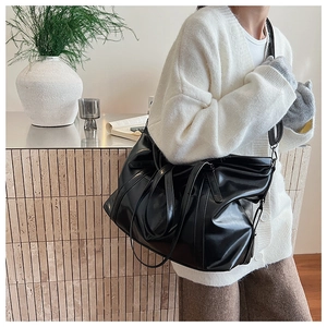 Detail of a large black glossy leather tote bag with soft texture and adjustable strap