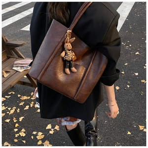 Detail of a dark brown vintage tote bag with a cute rabbit charm on an autumn street