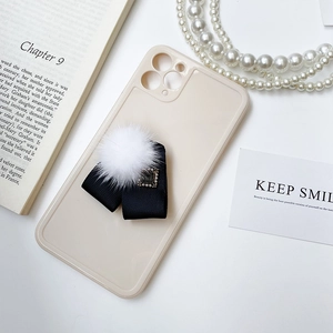 Détail de la coque beige avec un ruban noir élégant et un pompon en fourrure blanche