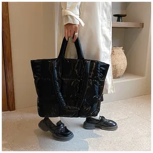Detail of a large black glossy quilted puffer tote bag with fashion label shown by a model