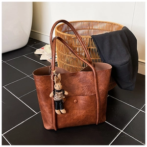 Brown tote bag with a vintage leather texture and a cute rabbit doll charm in a home setting