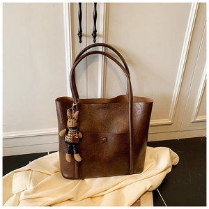 Detail of brown tote bag with retro lychee texture, front pocket and cute rabbit doll charm