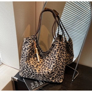 Detailed macro view of large leopard print tote bag with brown leather handles and bead charm