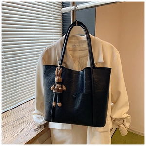 Close-up of black textured tote bag with a cute plush rabbit charm on a white coat