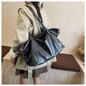 Close-up of black retro leather tote bag with elegant side pleats and buckle strap detail