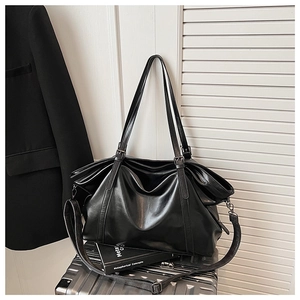 Détail d'un grand sac cabas noir posé sur une valise argentée pour les trajets