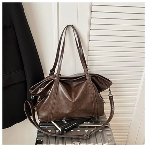 Detail of soft brown leather tote texture and adjustable strap on a metal suitcase