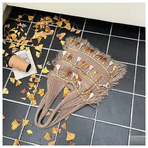 Flat lay of brown knit tote bag with boho tassels and autumn leaves on a dark surface