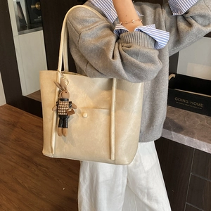 Large beige faux leather tote bag with rabbit charm shown on model in cozy home setting