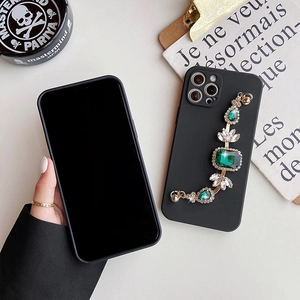 Detail view of black iPhone case with luxury emerald gemstone bracelet and gold chain