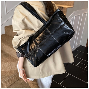 Detail of a large black quilted tote bag with glossy finish shown on shoulder in a lifestyle setting