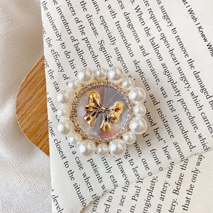 Detailed close-up of a golden bow phone grip with sparkling rhinestones and white pearls