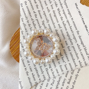 Macro shot of an elegant pearl-framed phone grip featuring a sparkling rhinestone butterfly