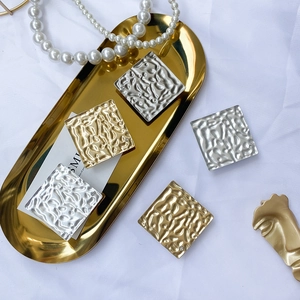 Macro shot of square metal earrings with irregular water ripples and small crystals