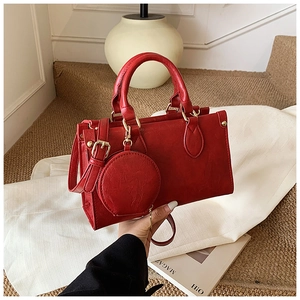 Detail of red pebbled leather handbag with gold buckles and mini round charm accessory
