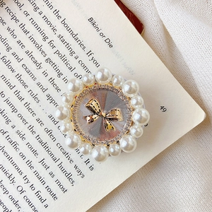 Detail of a luxury phone grip with a golden bow, pearls, and radiant silver texture