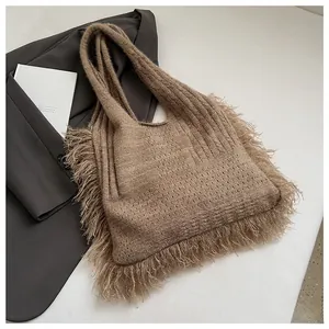 Detail shot of brown knitted tote bag with dense side fringes on a white marble surface