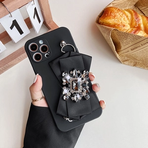 Detail of black bow iPhone case with crystal gemstone held by hand in warm setting