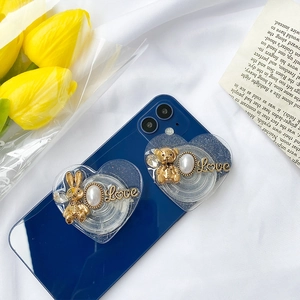 Macro detail of heart-shaped phone grip with gold rabbit and pearl on blue phone