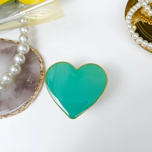 Detail view of heart-shaped green phone grip with gold trim on a white decorative surface
