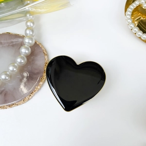 Glossy black heart-shaped jewelry tray with gold rim on a minimalist white background
