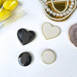 Detail of heart and round enamel phone grips with gold metal borders in black and white