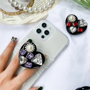 Close-up of heart-shaped phone grip with luxury rhinestones and pearls on black base