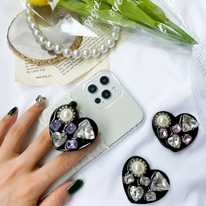 Detail of luxury heart-shaped phone grip with pearls and rhinestones on satin