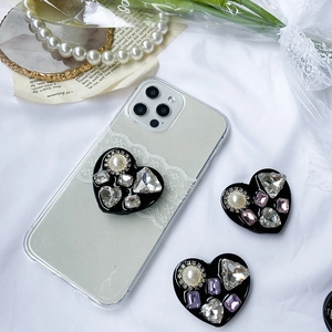 Detail of luxury rhinestone heart phone grip with large pearl on black base