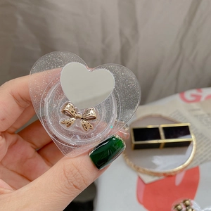 Detail of heart-shaped glitter phone grip with makeup mirror and gold bow accessory