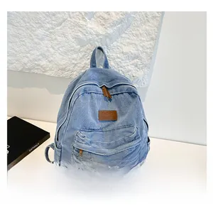 Detail of light blue washed denim backpack with brown leather zipper pulls and logo patch