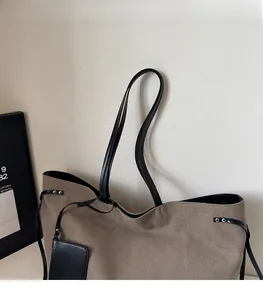 Dettaglio della borsa tote in tela grigia con spallacci in pelle nera e coulisse laterale