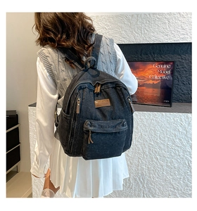 Close-up of black denim backpack with leather patch and washed fabric detail