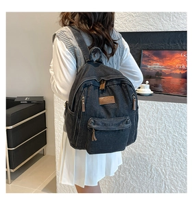Detail of black denim backpack featuring brown leather zipper pulls and multi-pocket design