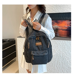 Detail of a vintage black denim backpack featuring multiple zipper pockets and leather pullers