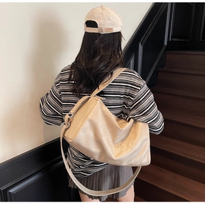 Close-up of large beige soft leather tote bag with embossed logo on a shoulder strap