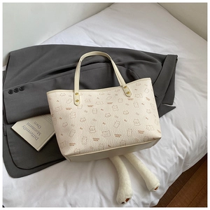 Close-up of cream tote bag with cute brown bear patterns and red bow ties on white bedding