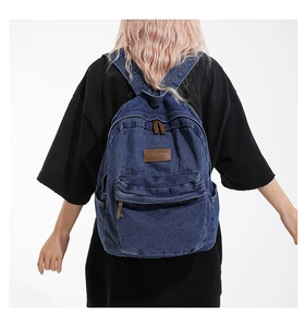 Detail of vintage blue denim backpack featuring leather logo patch and large front pocket