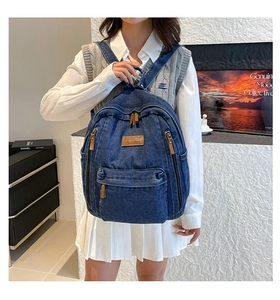 Macro detail of dark blue denim backpack with leather logo and zipper pockets